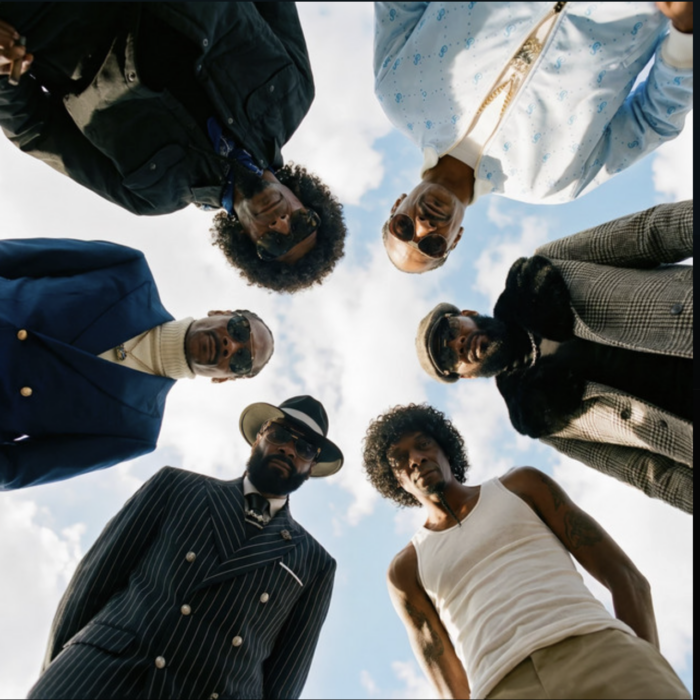 Snoop Dogg and artists in a circular low-angle group portrait against a sky background.